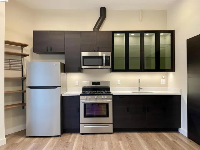 Kitchen with stainless steel appliances, light countertops, light wood finished floors, and glass fronted cabinets