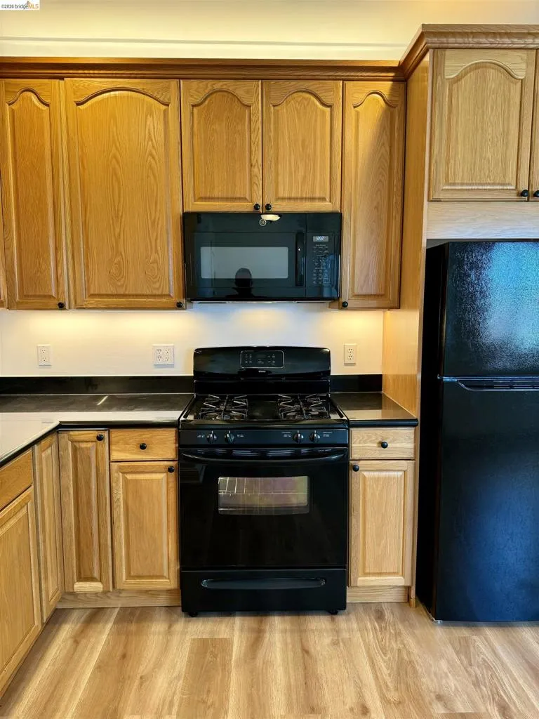 Kitchen with black appliances, dark countertops, light wood-style floors, and wood finish cabinetry