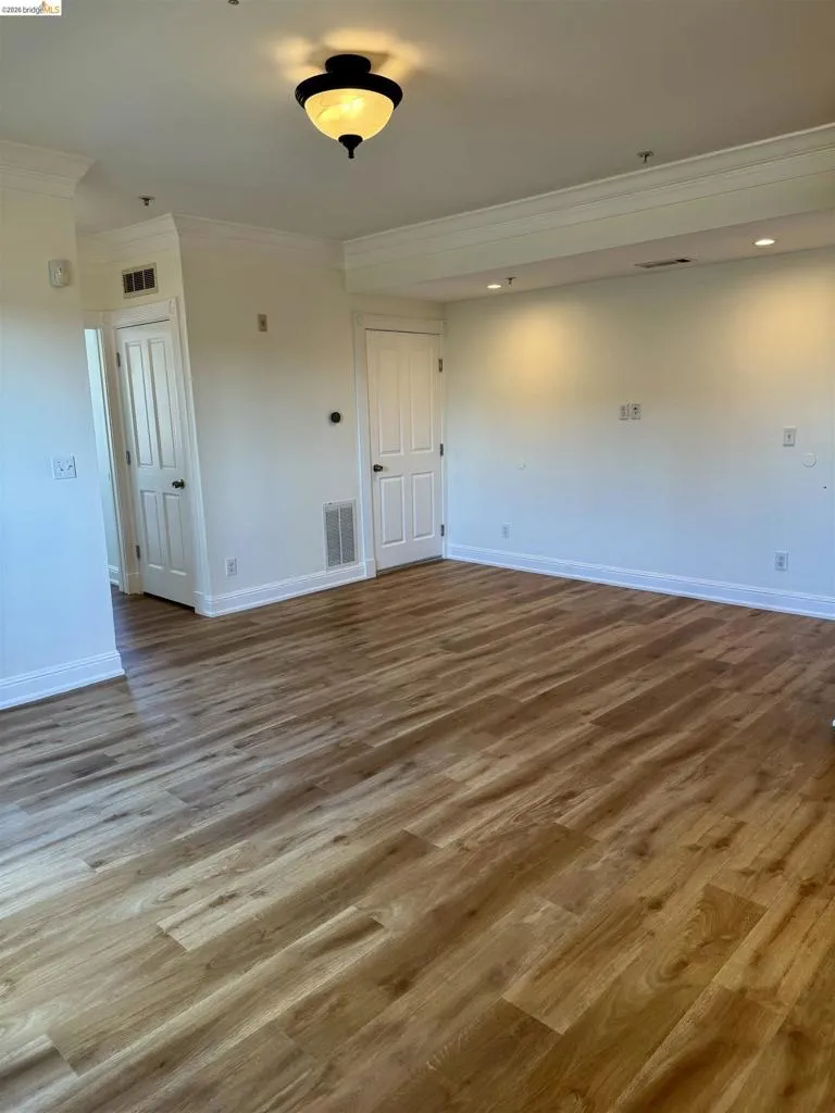 Empty room featuring dark wood-style floors and ornamental molding