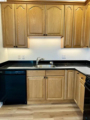 Kitchen with dark countertops, black appliances, and light wood finished floors