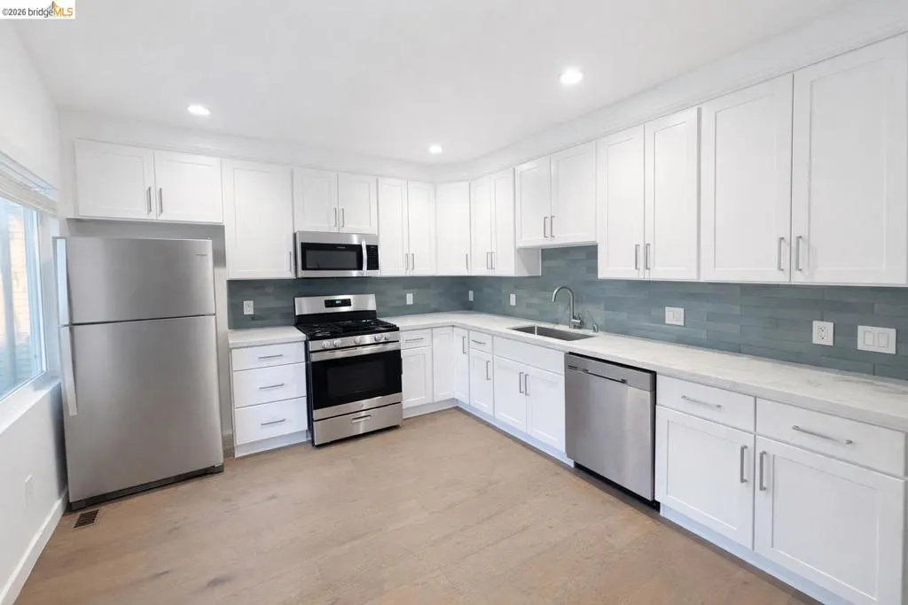 Kitchen with stainless steel appliances, white cabinetry, light wood-style floors, backsplash, and light stone countertops