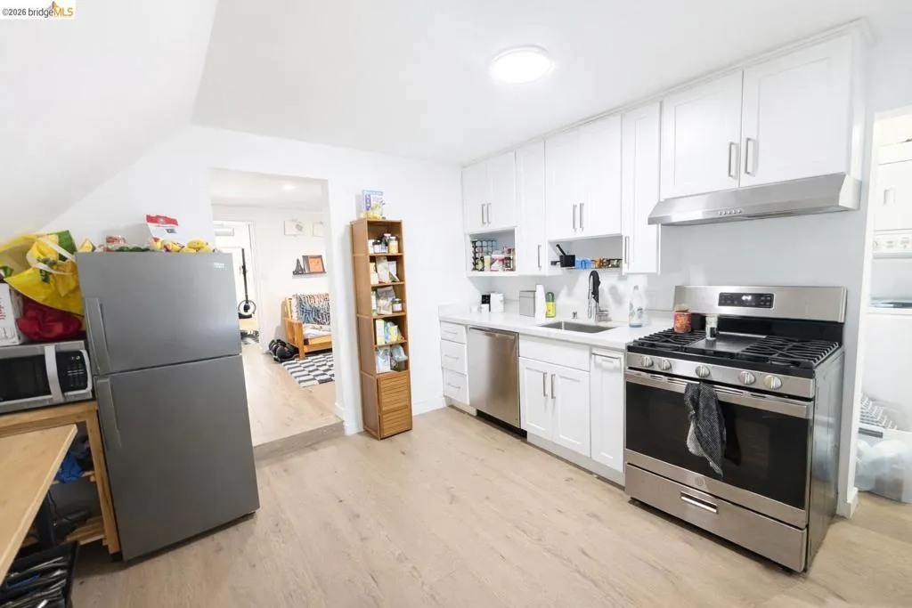 Kitchen with stainless steel appliances, white cabinetry, light wood-style floors, and open shelves