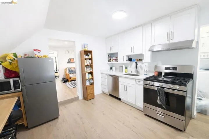 Kitchen with stainless steel appliances, white cabinetry, light wood-style floors, and open shelves