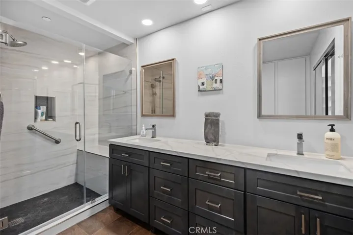 Remodeled bathroom with new vanities, quartz countertops and frameless shower enclosure with a seat.