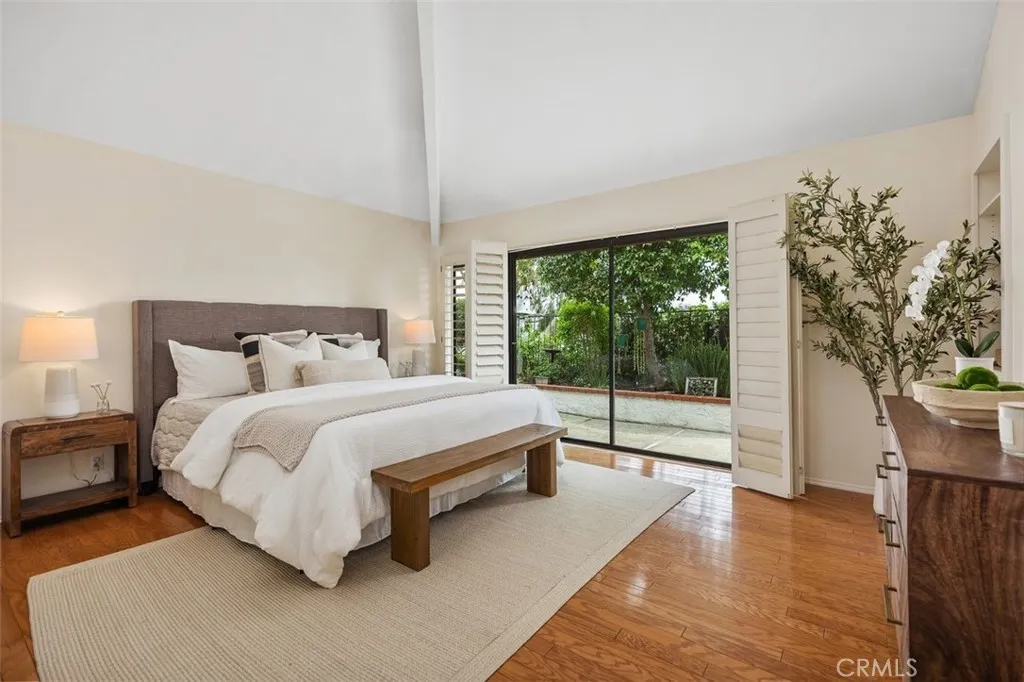 The primary bedroom includes vaulted ceilings and a sliding glass door leading outside to the garden with plenty of natural light.