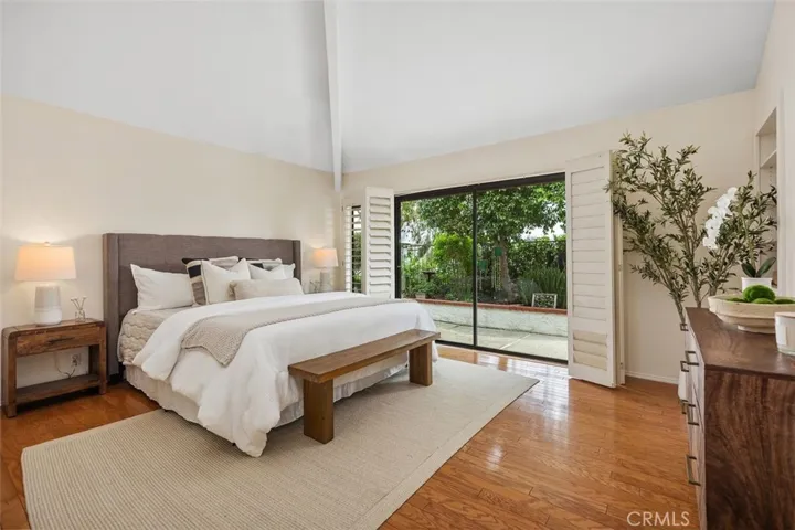 The primary bedroom includes vaulted ceilings and a sliding glass door leading outside to the garden with plenty of natural light.