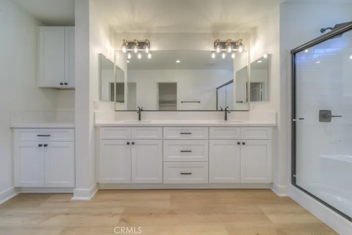 The primary bathroom offers plenty of storage, real wood cabinetry, quartz countertops, black hardware, extra vanity space, and a private toilet area.