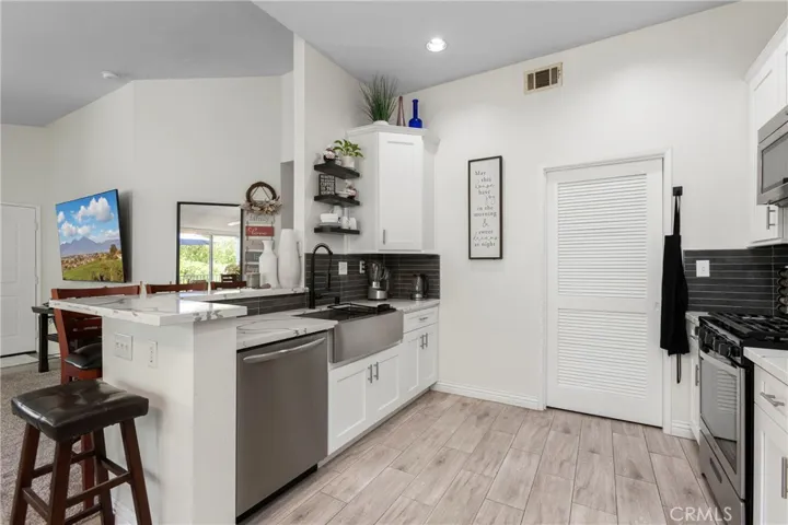 Recently remodeled kitchen with white cabinetry, quarts counters, a farmhouse sink, and stainless steel appliances