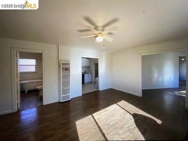Unfurnished bedroom featuring dark wood-style floors, a heating unit, connected bathroom, and ceiling fan