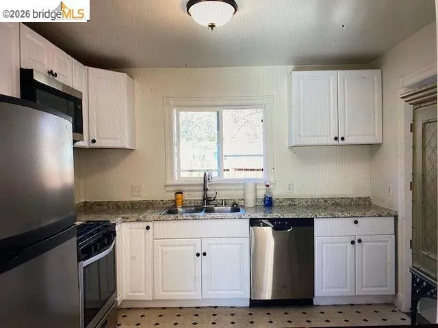 Kitchen featuring stainless steel appliances, white cabinets, light floors, and light stone countertops