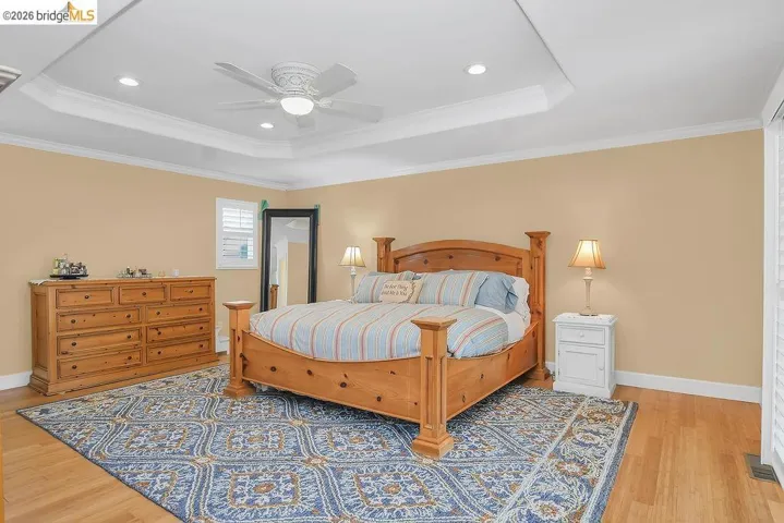 Bedroom featuring crown molding, light wood-type flooring, ceiling fan, a raised ceiling, and recessed lighting