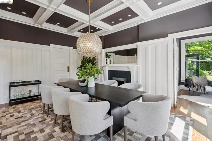 Dining area with a fireplace, a decorative wall, hanging lights, coffered ceiling, and light wood-style flooring