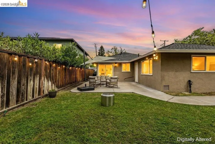 Back of house at dusk with outdoor furniture, stucco siding, a patio, a fenced backyard, and a shingled roof