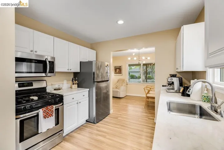 Kitchen with stainless steel appliances, light countertops, white cabinets, suspended lighting, and light wood-style flooring