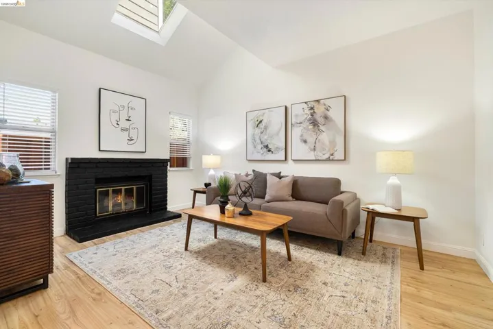 Living area featuring vaulted ceiling, plenty of natural light, a skylight, a fireplace, and light wood-style flooring