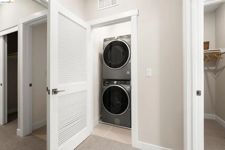 Laundry room with stacked washer and clothes dryer and light tile patterned flooring