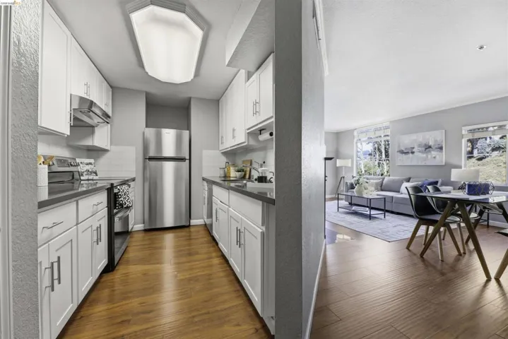 Kitchen with stainless steel appliances, white cabinets, dark countertops, dark wood-type flooring, and open floor plan