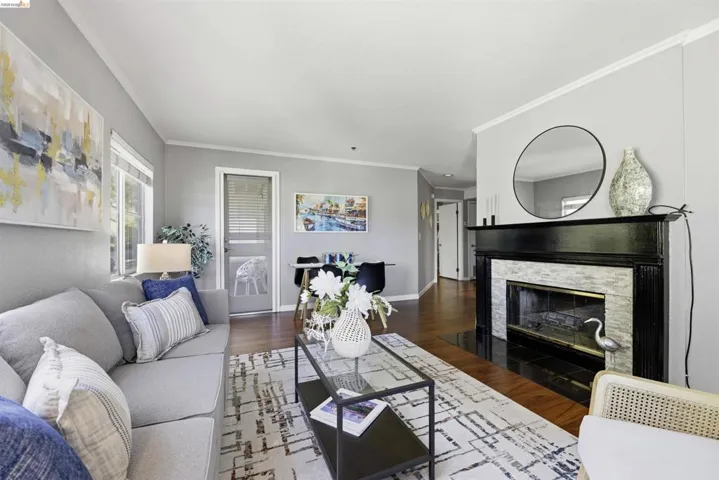 Living room with dark wood finished floors, ornamental molding, and a stone fireplace