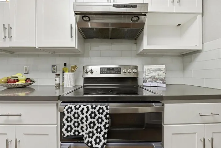 Kitchen featuring stainless steel electric range, range hood, white cabinetry, and backsplash