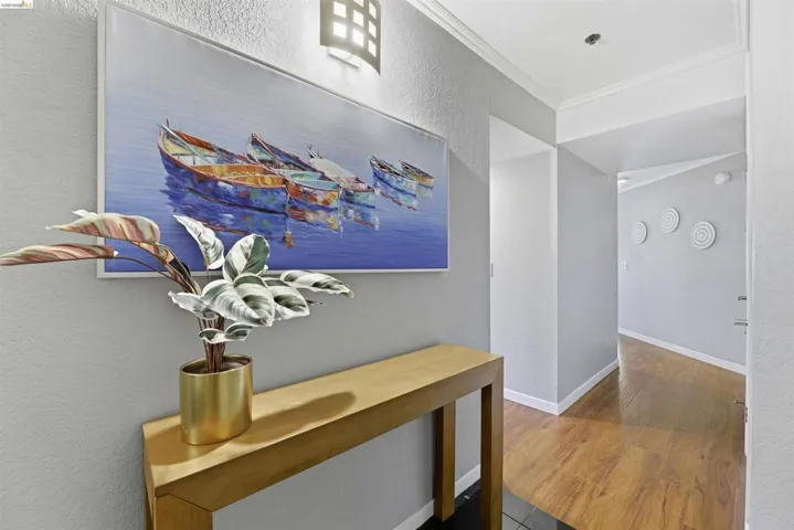 Corridor featuring a textured wall, crown molding, and dark wood-type flooring