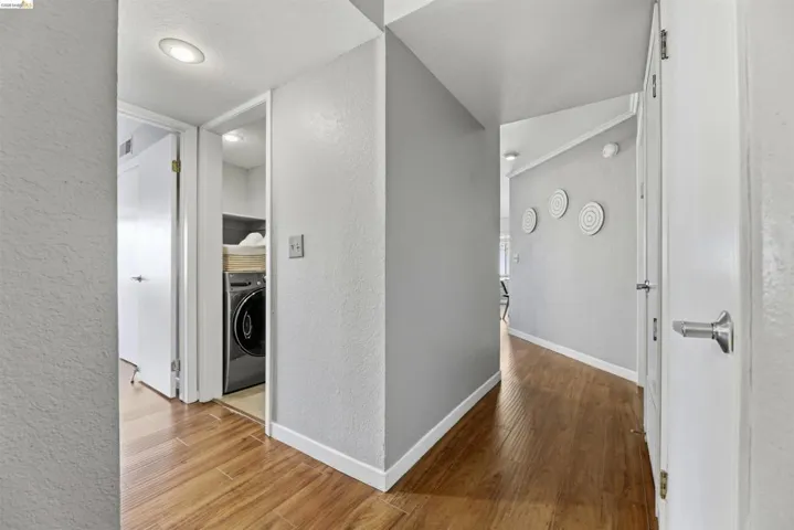 Hall with a textured wall, light wood-style flooring, washer / clothes dryer, and a textured ceiling