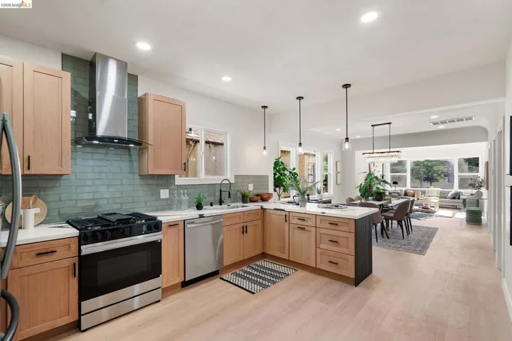 Kitchen with appliances with stainless steel finishes, wall chimney range hood, a peninsula, hanging light fixtures, and light wood-type flooring