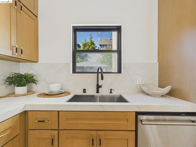 Kitchen featuring stainless steel dishwasher, backsplash, and light stone counters