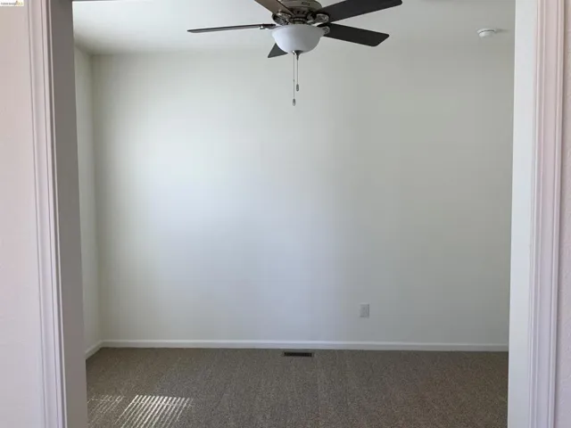 Empty room with dark colored carpet and a ceiling fan