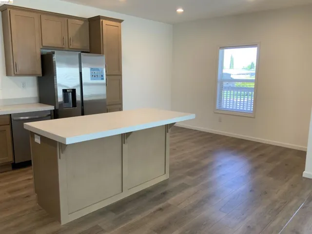 Kitchen featuring stainless steel appliances, light countertops, dark wood-style floors, a kitchen island, and a kitchen breakfast bar