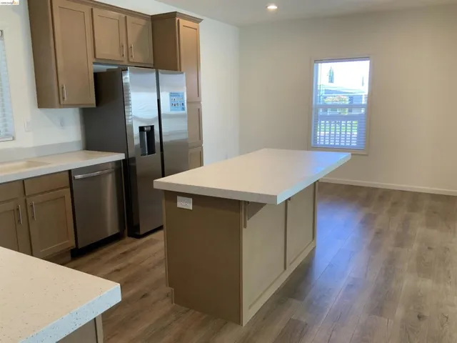 Kitchen with a center island, dark wood-type flooring, stainless steel appliances, light countertops, and recessed lighting