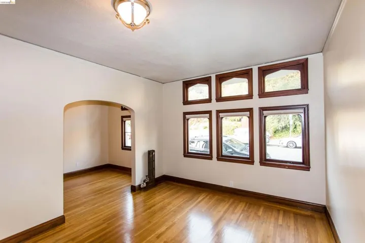 Empty room with arched walkways, wood-type flooring, radiator heating unit, and ornamental molding