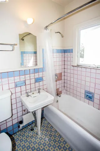 Full bath with tile walls, shower / bath combo with shower curtain, and a wainscoted wall