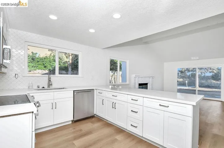 Kitchen featuring a peninsula, a brick fireplace, light wood finished floors, stainless steel appliances, and white cabinetry