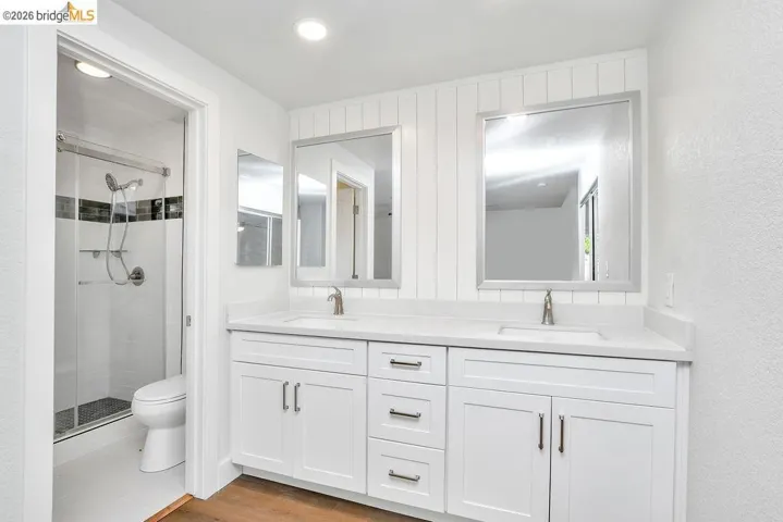 Full bath with double vanity, a stall shower, wood finished floors, and recessed lighting