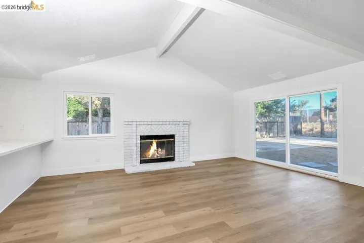 Unfurnished living room featuring light wood-type flooring, beam ceiling, and a brick fireplace
