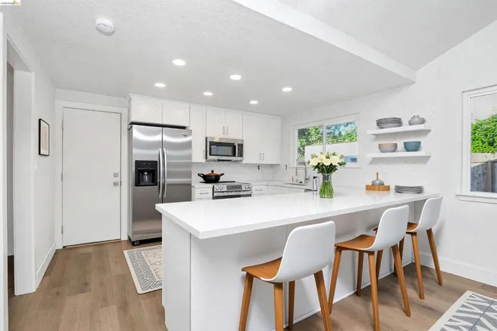 Kitchen with a peninsula, white cabinets, stainless steel appliances, open shelves, and a kitchen bar