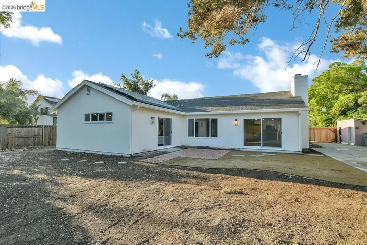 Rear view of property with a patio, solar panels, stucco siding, a chimney, and a fenced backyard