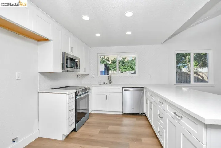 Kitchen featuring white cabinets, stainless steel appliances, a textured ceiling, light wood-style floors, and decorative backsplash