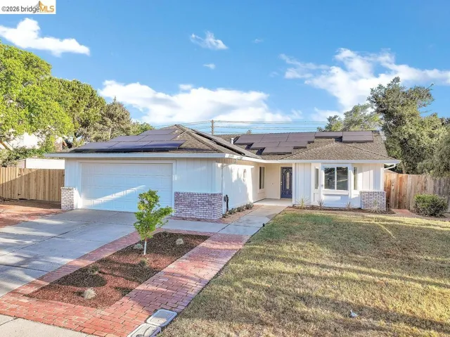 Ranch-style house with brick siding, roof mounted solar panels, driveway, and a garage