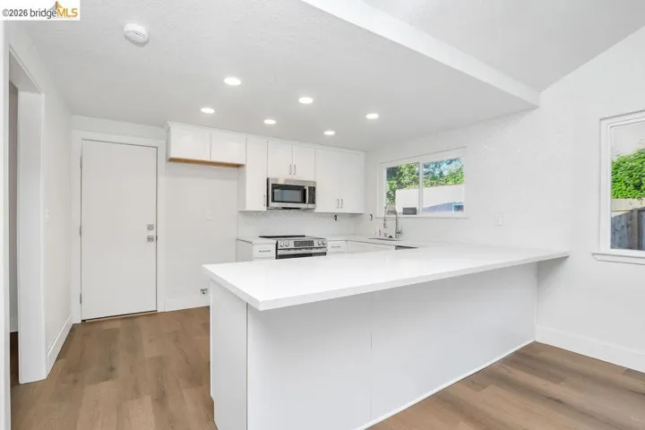Kitchen with a peninsula, white cabinets, light wood-style floors, stainless steel appliances, and decorative backsplash