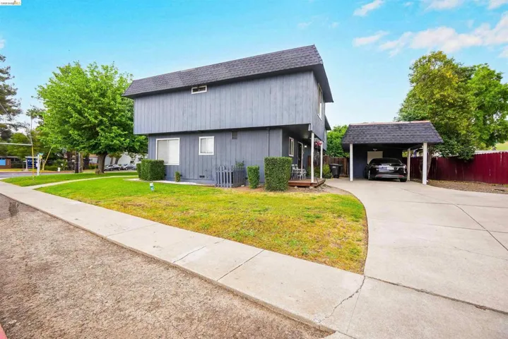 View of side of home with roof with shingles, driveway, and a carport