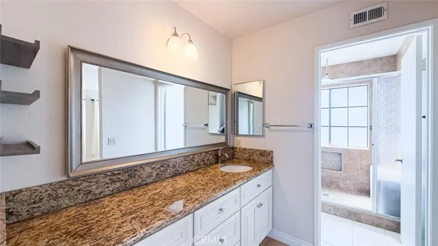The primary bathroom with granite countertop and white cabinets with private door for the walk-in shower with glass doors.