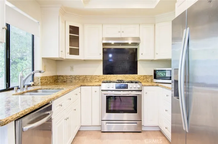The remodeled kitchen with granite countertop, white cabinets and stainless steel appliances including refrigerator.