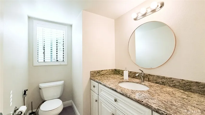 The downstair powder room with granite countertop and white cabinets as well as a window.