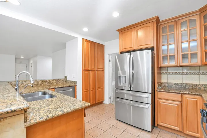 Kitchen with stainless steel appliances, glass insert cabinets, light stone countertops, light tile patterned floors, and recessed lighting
