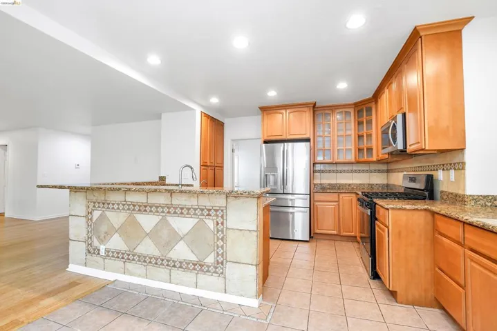 Kitchen featuring light stone counters, stainless steel appliances, glass insert cabinets, light tile patterned flooring, and recessed lighting