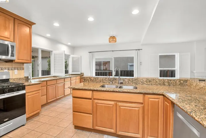 Kitchen featuring stainless steel appliances, light stone countertops, backsplash, recessed lighting, and light tile patterned floors