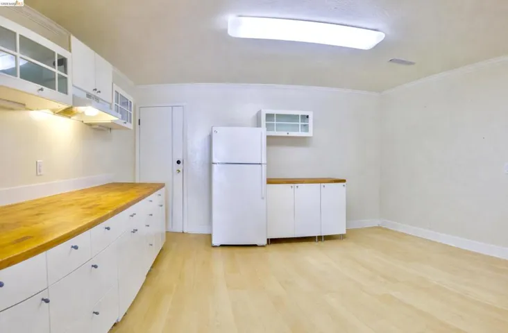 Kitchen with white cabinets, butcher block countertops, freestanding refrigerator, glass insert cabinets, and light wood-type flooring