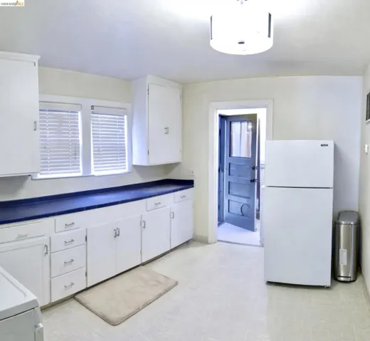 Kitchen with freestanding refrigerator, light floors, white cabinetry, and dark countertops