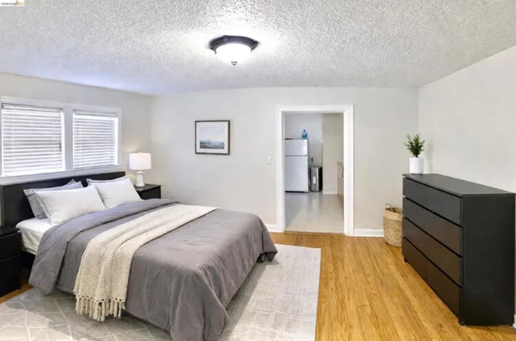 Bedroom featuring freestanding refrigerator, light wood finished floors, and a textured ceiling